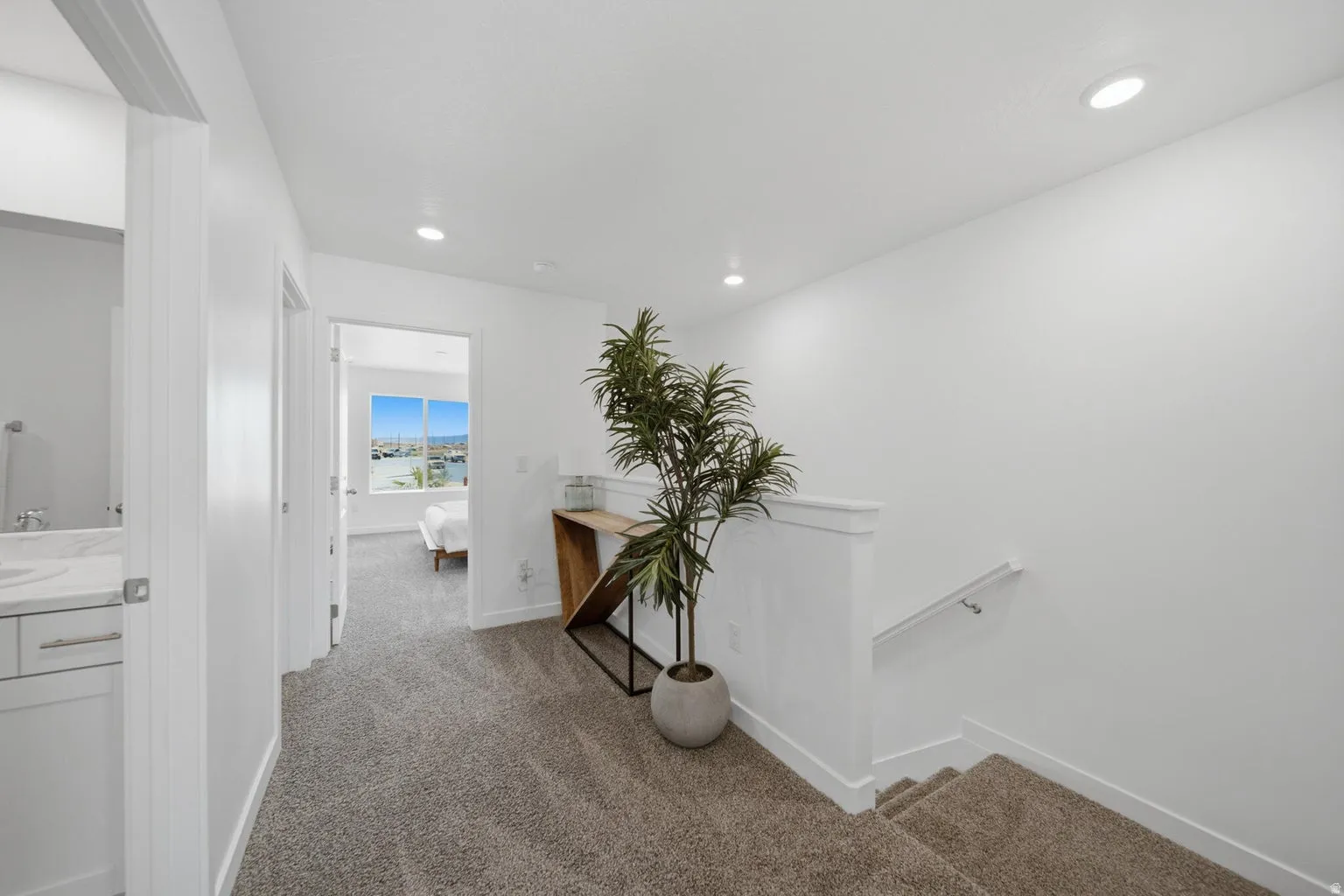 Carpeted hallway with recessed lighting and a white handrail