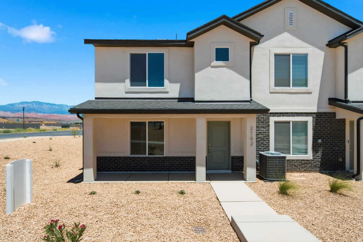 Two-story residence featuring a covered entry, stucco and brick veneer exterior, and a concrete pathway