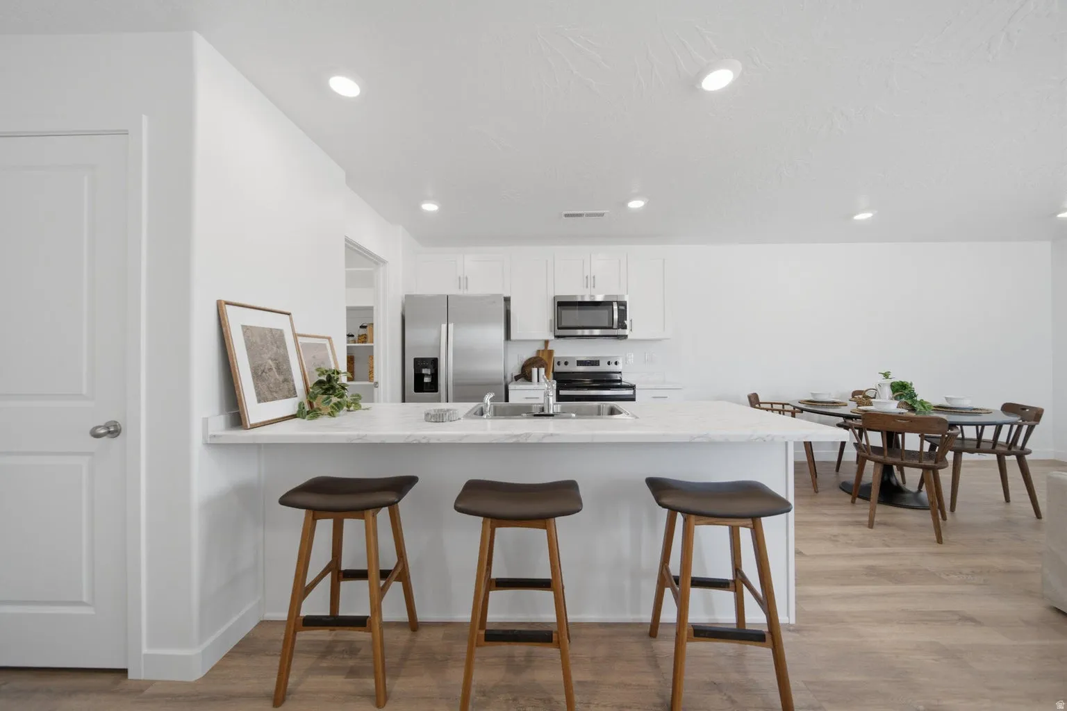 Open-concept kitchen featuring an island with counter seating, stainless steel appliances, white cabinetry, and wood-finish flooring
