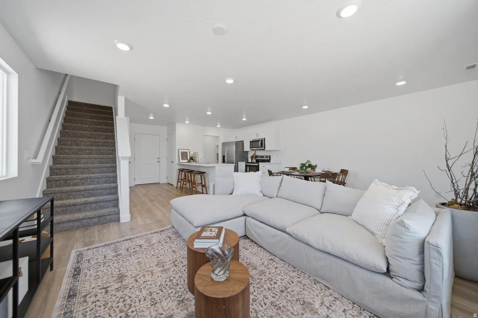 Open-concept living space with wood-finish flooring, recessed lighting, and a white kitchen featuring stainless steel appliances