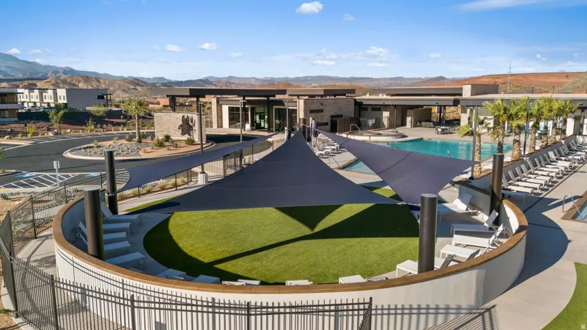 Outdoor amphitheater with artificial turf, multiple shade sails, and surrounding pool deck