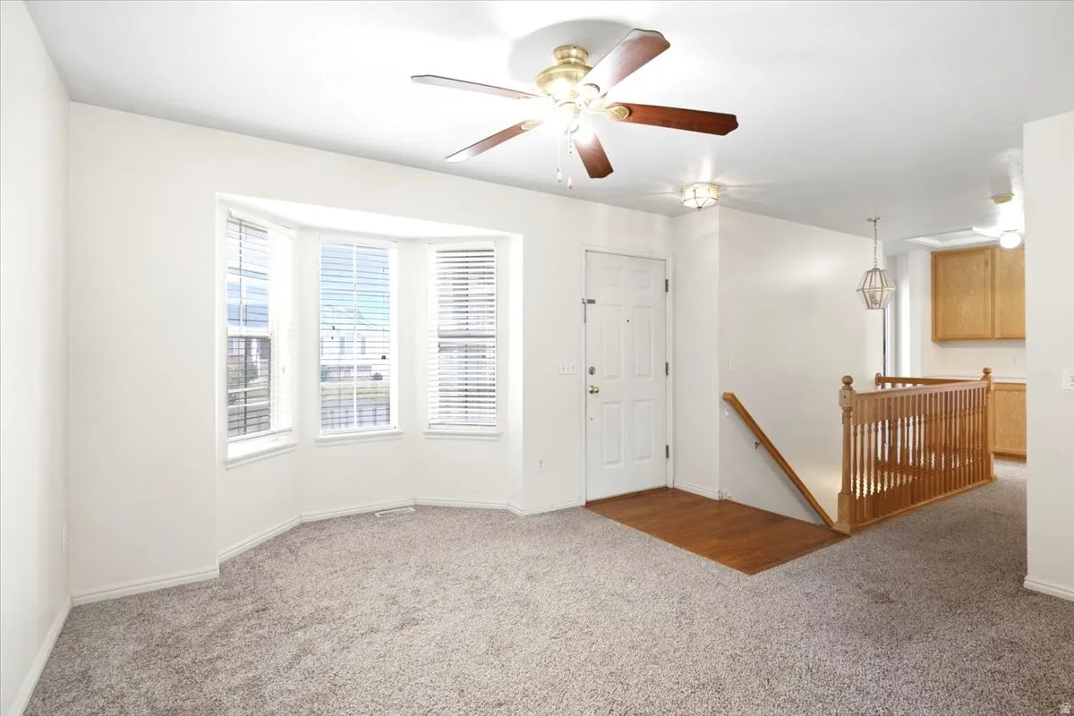 Bay window with blinds, ceiling fan, wood-finish flooring at entry, and wood railing with balusters