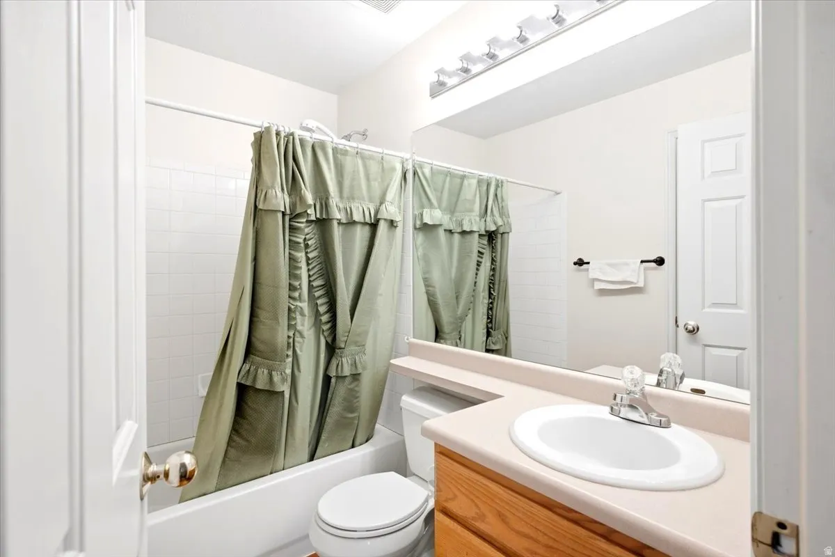 Full bathroom featuring a white porcelain tub and shower combination with white subway tile surround, a single vanity with wood-finish cabinetry, a built-in countertop, and an integrated mirror with overhead vanity lighting