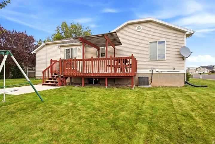 Expansive backyard featuring a wood-tone deck with stairs, a patio area, and a green lawn