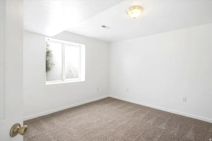 White painted walls, neutral tone carpet flooring, flush mount ceiling light fixture, and a single window