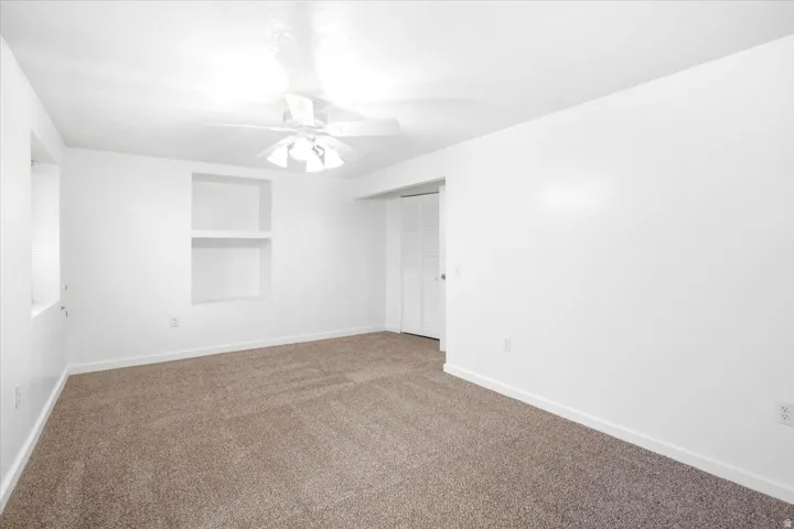 Neutral tone wall paint, built-in shelving, carpet flooring, ceiling fan, and bi-fold closet doors