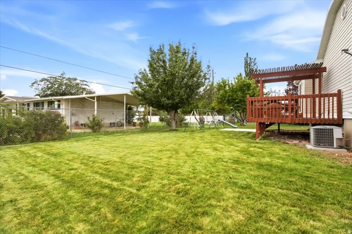 Expansive backyard featuring a manicured lawn, a raised wood deck with a pergola, and a covered carport structure