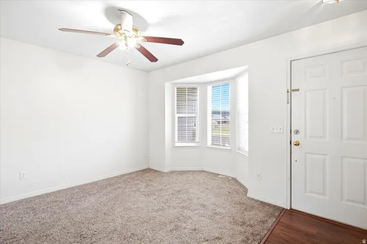Bay window with blinds, ceiling fan with light fixture, carpeted flooring, and wood-finish flooring at entry