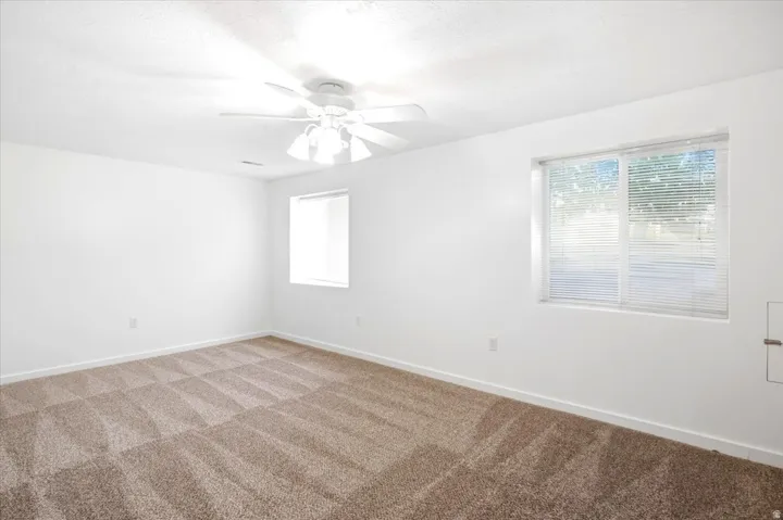 Recessed lighting, ceiling fan, two windows with blinds, and neutral carpeting