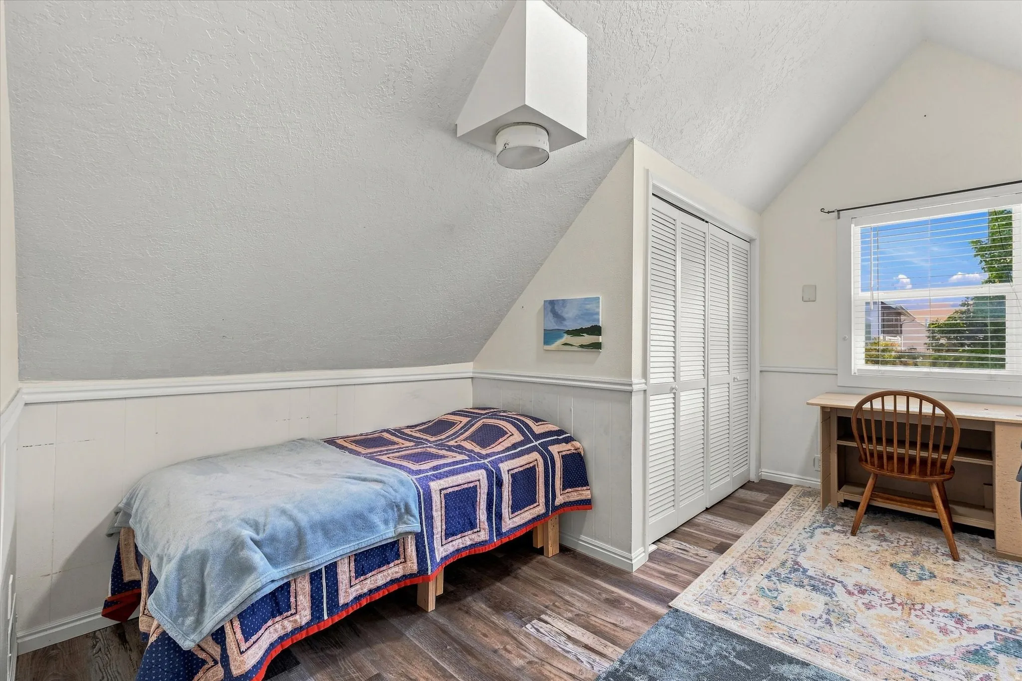 Sloped ceiling architectural detail, wood-finish flooring, window with natural illumination, built-in louvered closet, and wainscoting