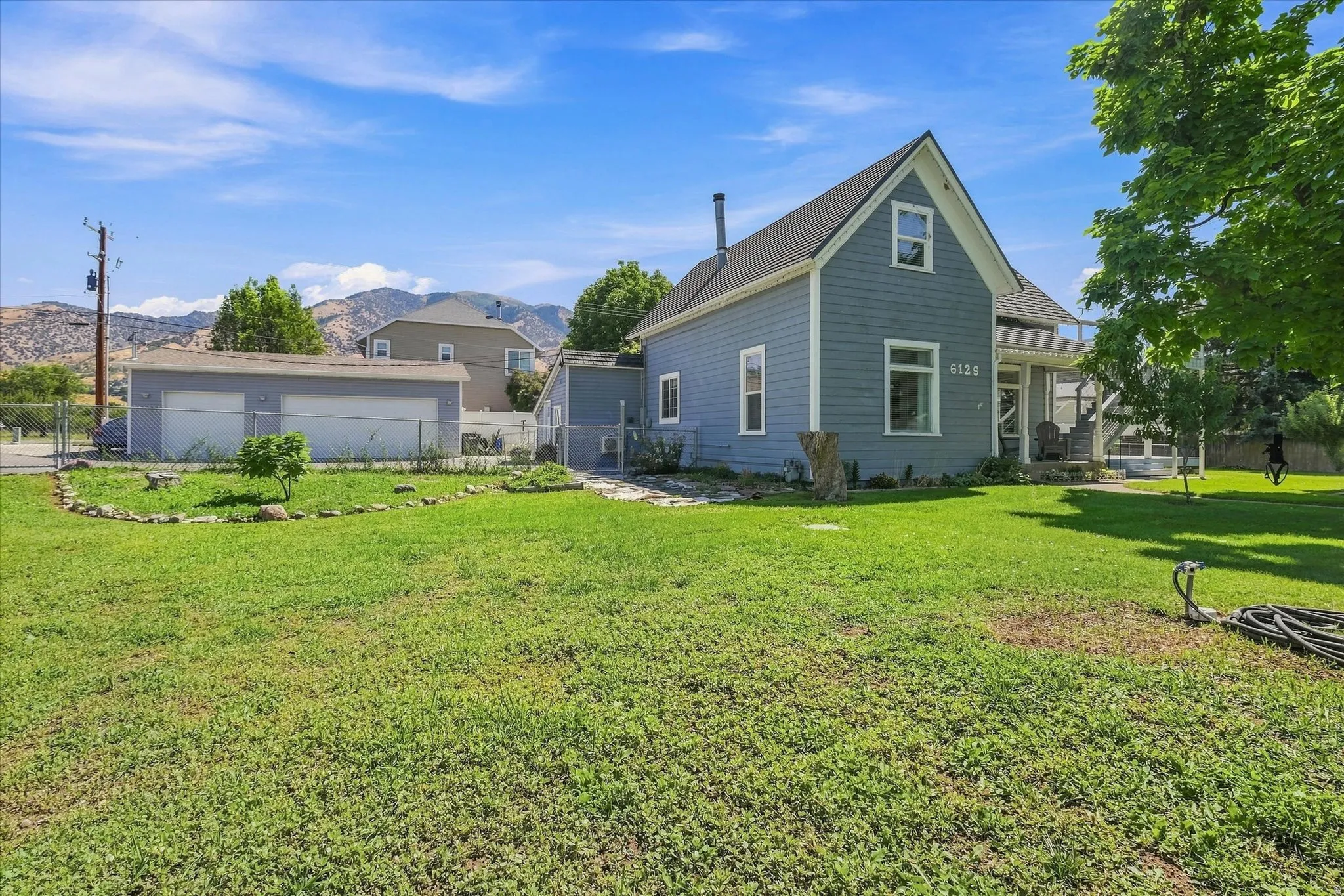 Two-story property with gray siding and white trim, featuring an attached covered porch, a separate two-car garage, and a expansive grassy yard