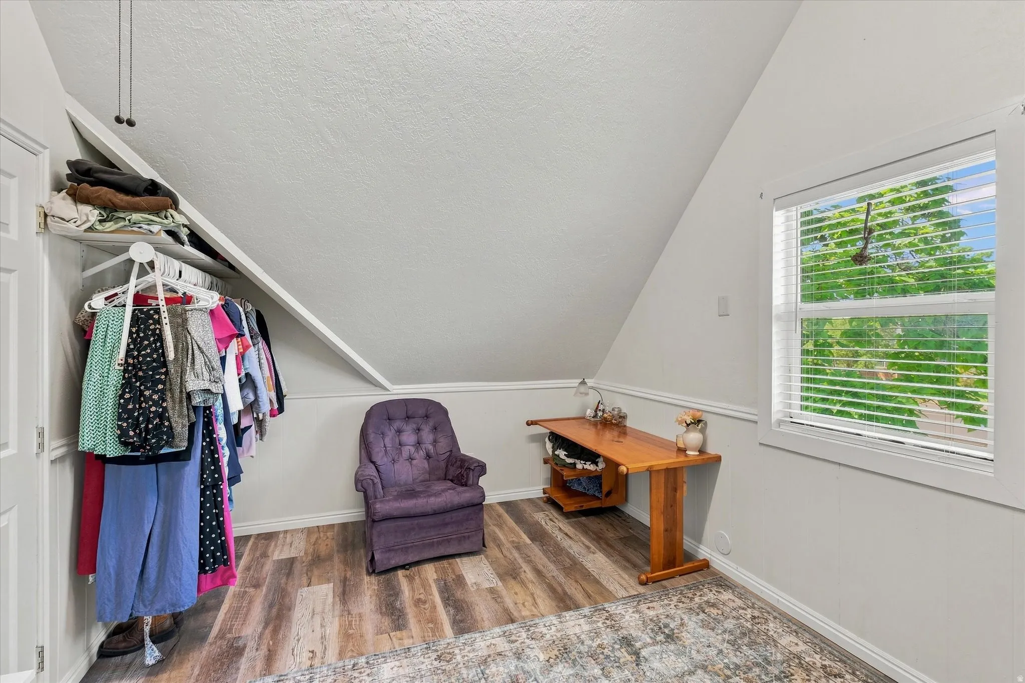 Sloped ceiling with recessed storage, wood-finish flooring, and natural light