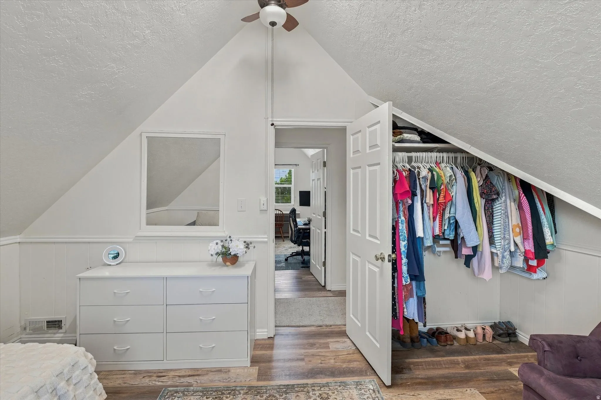 Vaulted ceiling with an overhead fan, wood-finish flooring, and sloped ceiling design