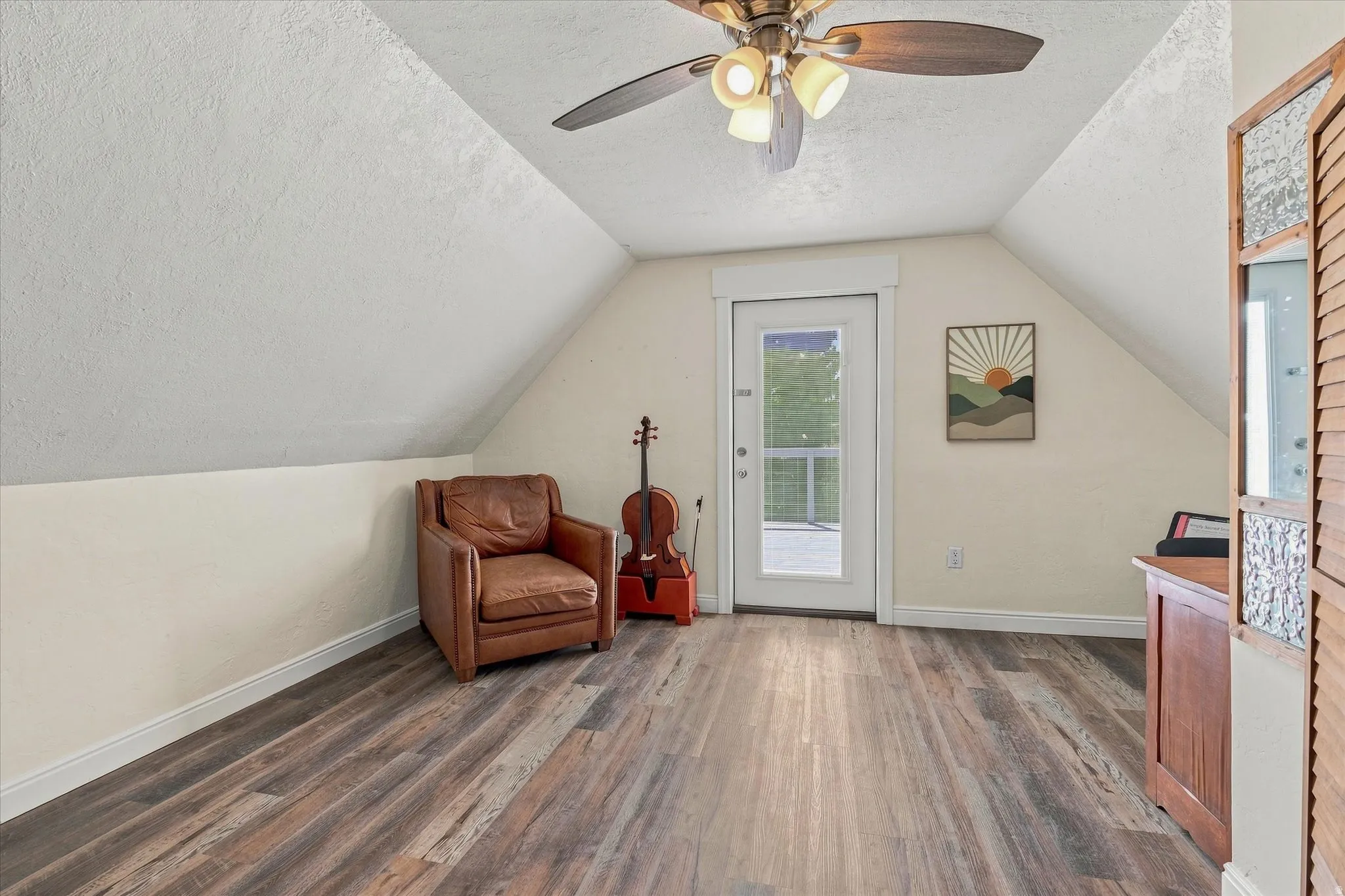 Vaulted ceiling with a ceiling fan, wood-finish flooring, and a glass-paneled door