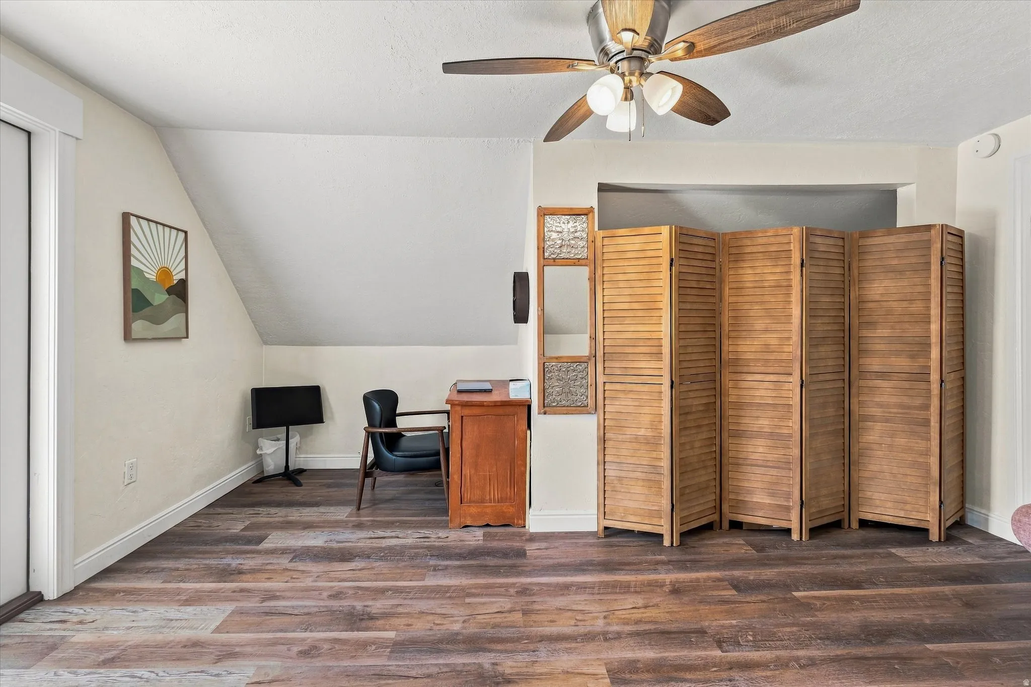 Spacious room with wood-finish flooring, an angled ceiling, and a ceiling fan with integrated lighting