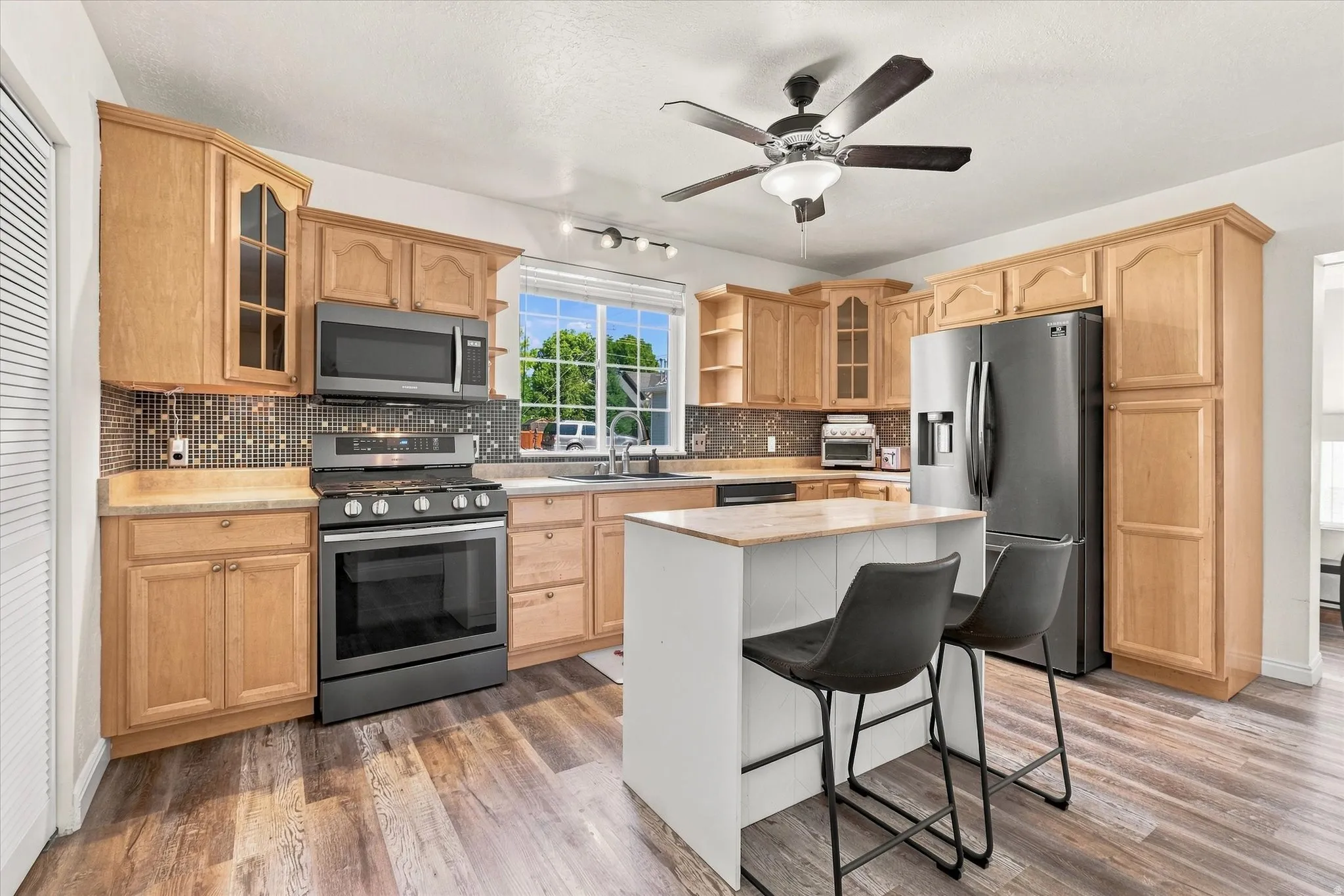 Well-appointed kitchen featuring wood cabinetry, stainless steel appliances, a center island with countertop seating, mosaic tile backsplash, and wood-finish flooring