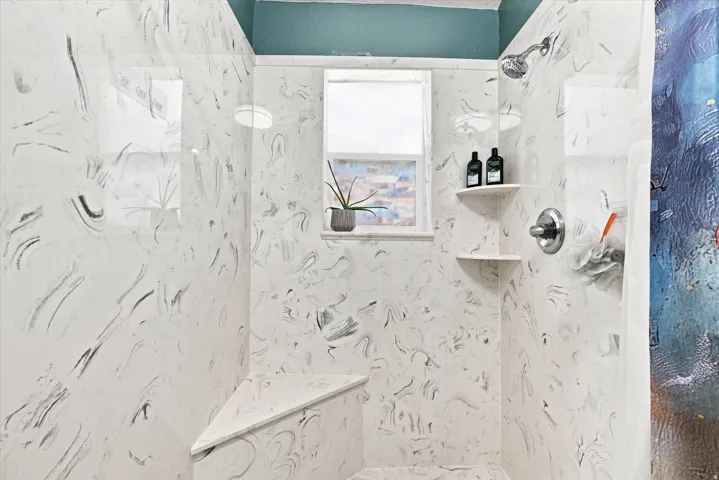 Shower enclosure with patterned wall panels, a built-in shower bench, and integrated corner shelving