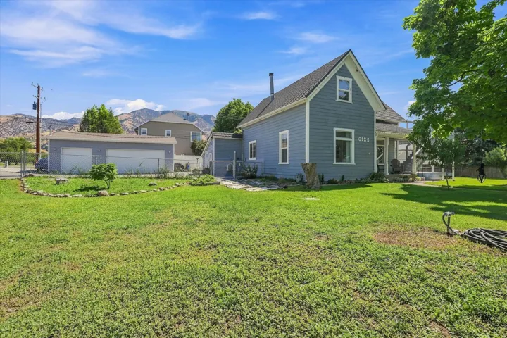 Two-story property with gray siding and white trim, featuring an attached covered porch, a separate two-car garage, and a expansive grassy yard