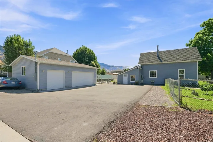 Two-car detached garage, asphalt driveway, gravel pathway, chain link fencing, and a separate structure with a shed roof