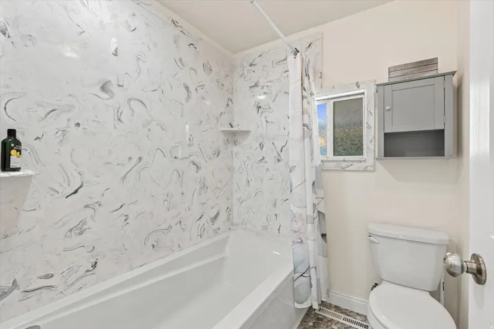 White bathtub with integrated shelving, patterned shower surround, and a wall-mounted storage cabinet