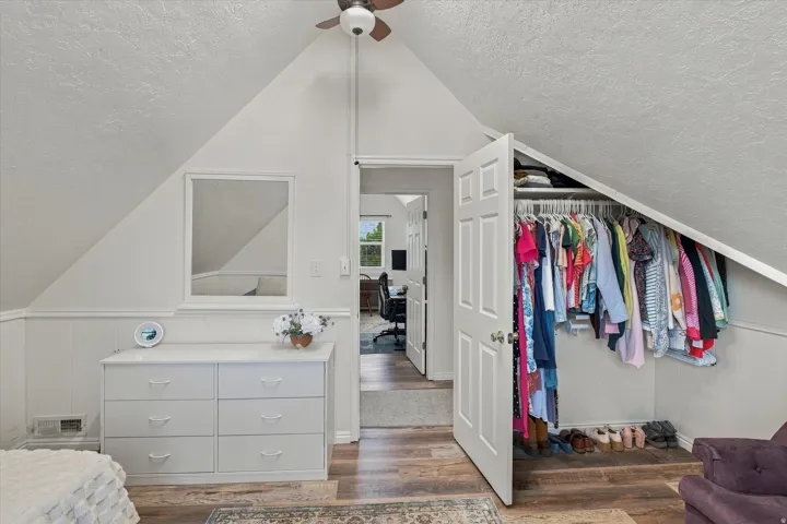 Vaulted ceiling with an overhead fan, wood-finish flooring, and sloped ceiling design