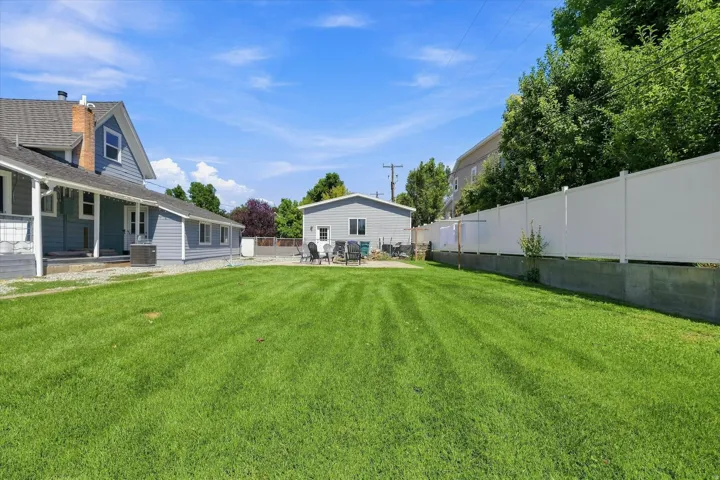 Expansive green lawn, detached outbuilding, white privacy fence, and paved patio area