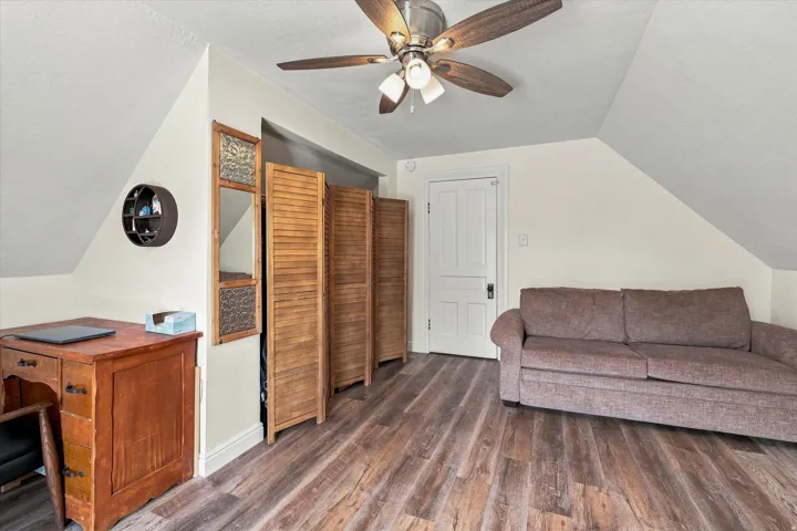Wood-finish flooring throughout, ceiling fan with light fixture, and white painted door with dark hardware