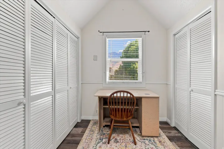 Vaulted ceiling with a window, wood-finish flooring, and slatted closet doors