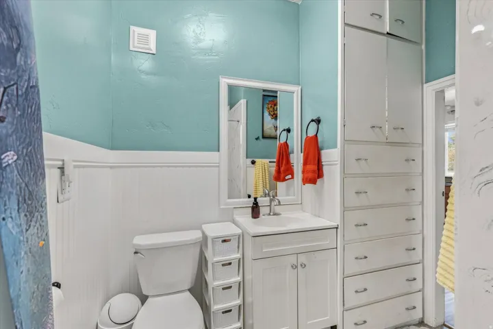 Bathroom featuring beadboard wainscoting, a vanity with a white countertop, a wall-mounted mirror, and extensive built-in cabinetry with drawers