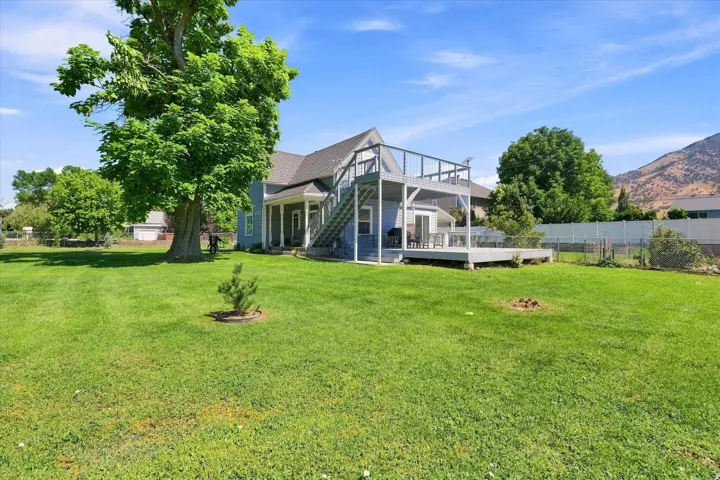 Expansive green lawn with mature trees, a multi-level deck, and a mountain backdrop