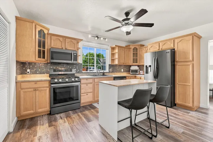 Well-appointed kitchen featuring wood cabinetry, stainless steel appliances, a center island with countertop seating, mosaic tile backsplash, and wood-finish flooring