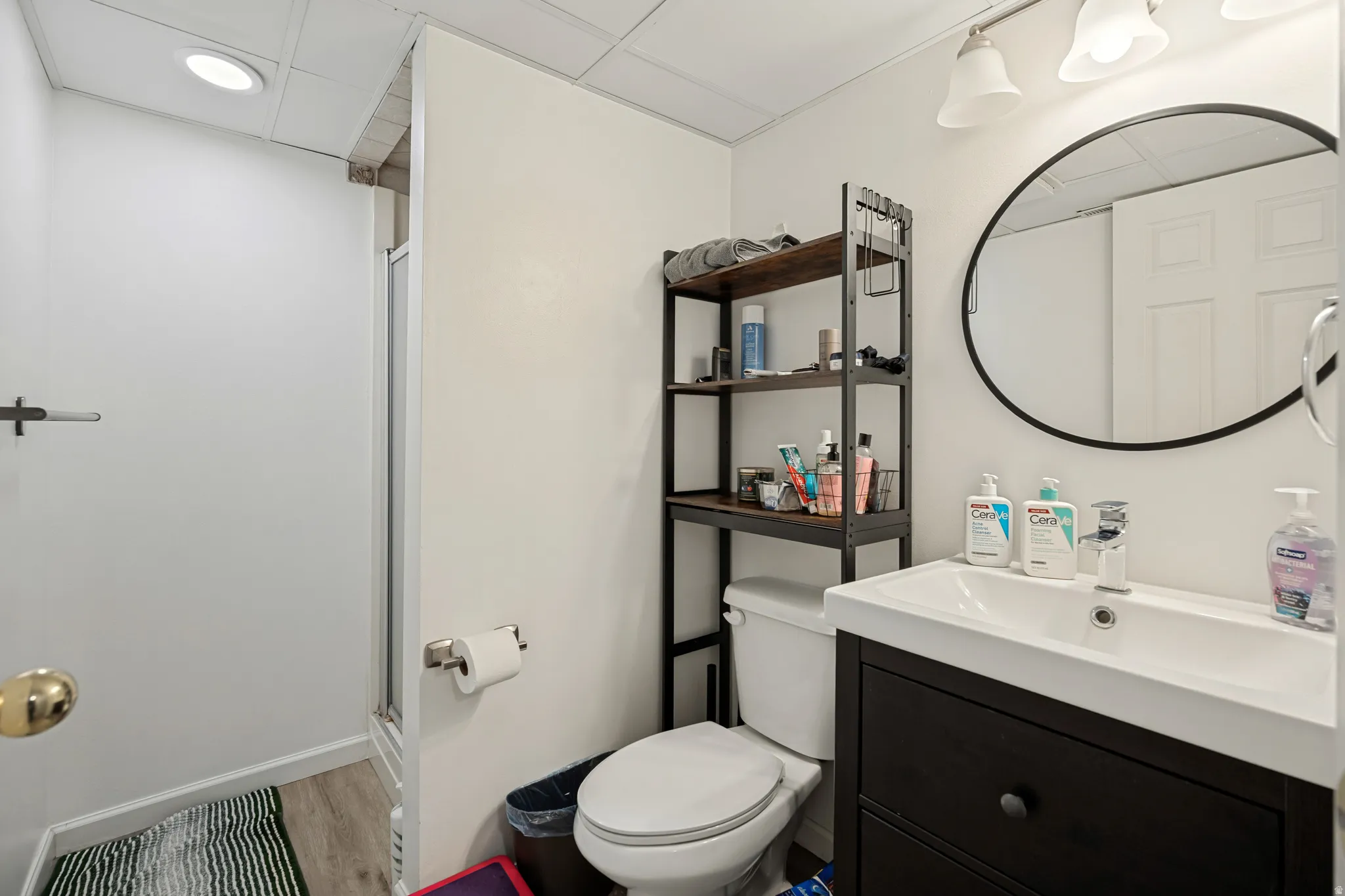 6711 - Basement Bathroom featuring a vanity with an integrated sink, round framed mirror, a three-light fixture, and a walk-in shower with a glass enclosure