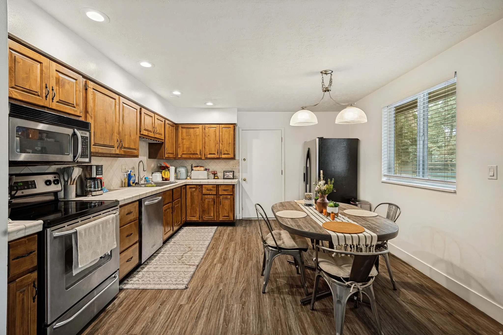 6711 - Kitchen featuring wood cabinetry, stainless steel appliances, wood-finish flooring, recessed lighting, and a window with blinds