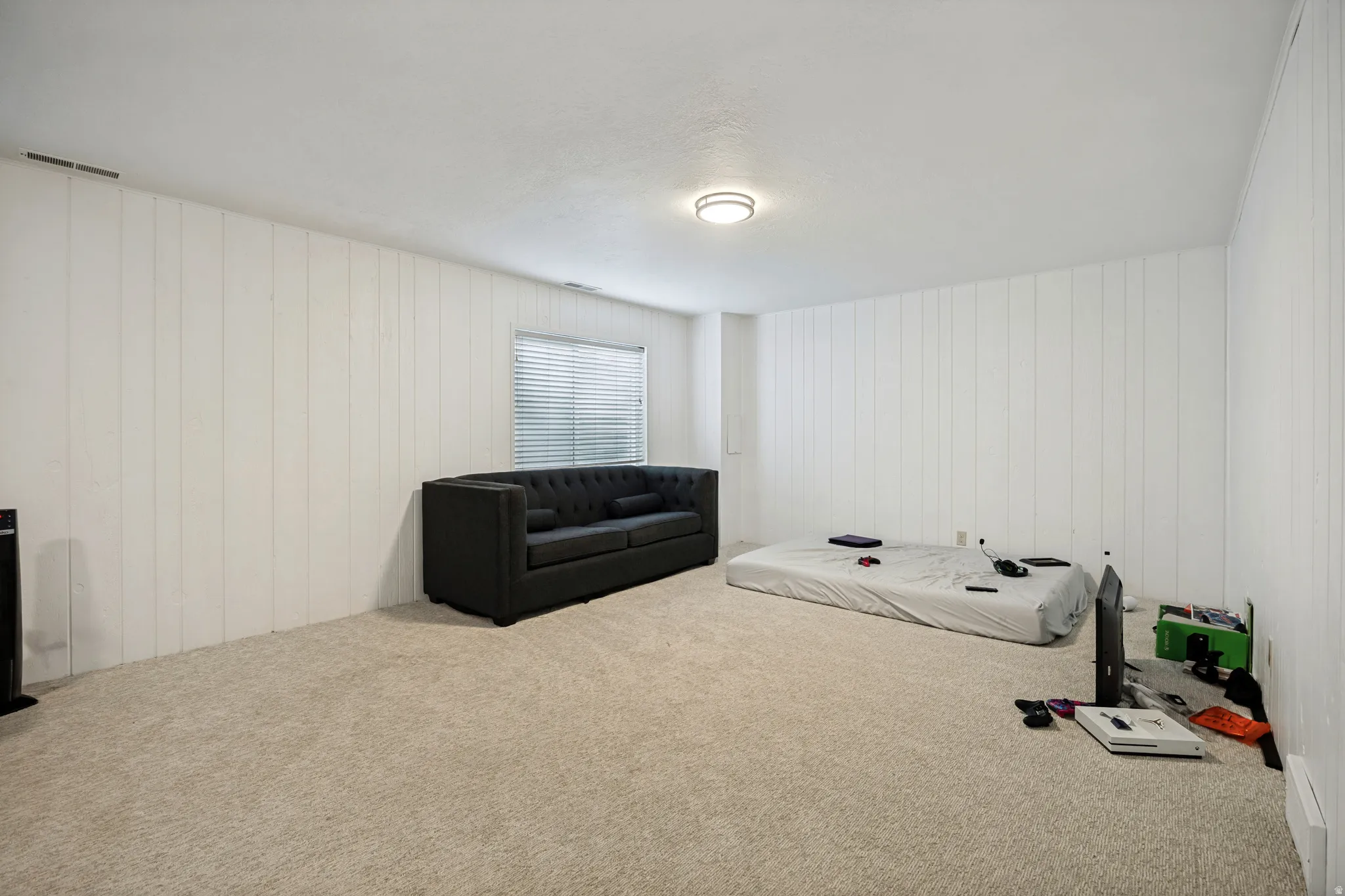 6711 - Basement Living Room. White paneling walls, neutral tone carpet, recessed lighting, and a single window with blinds