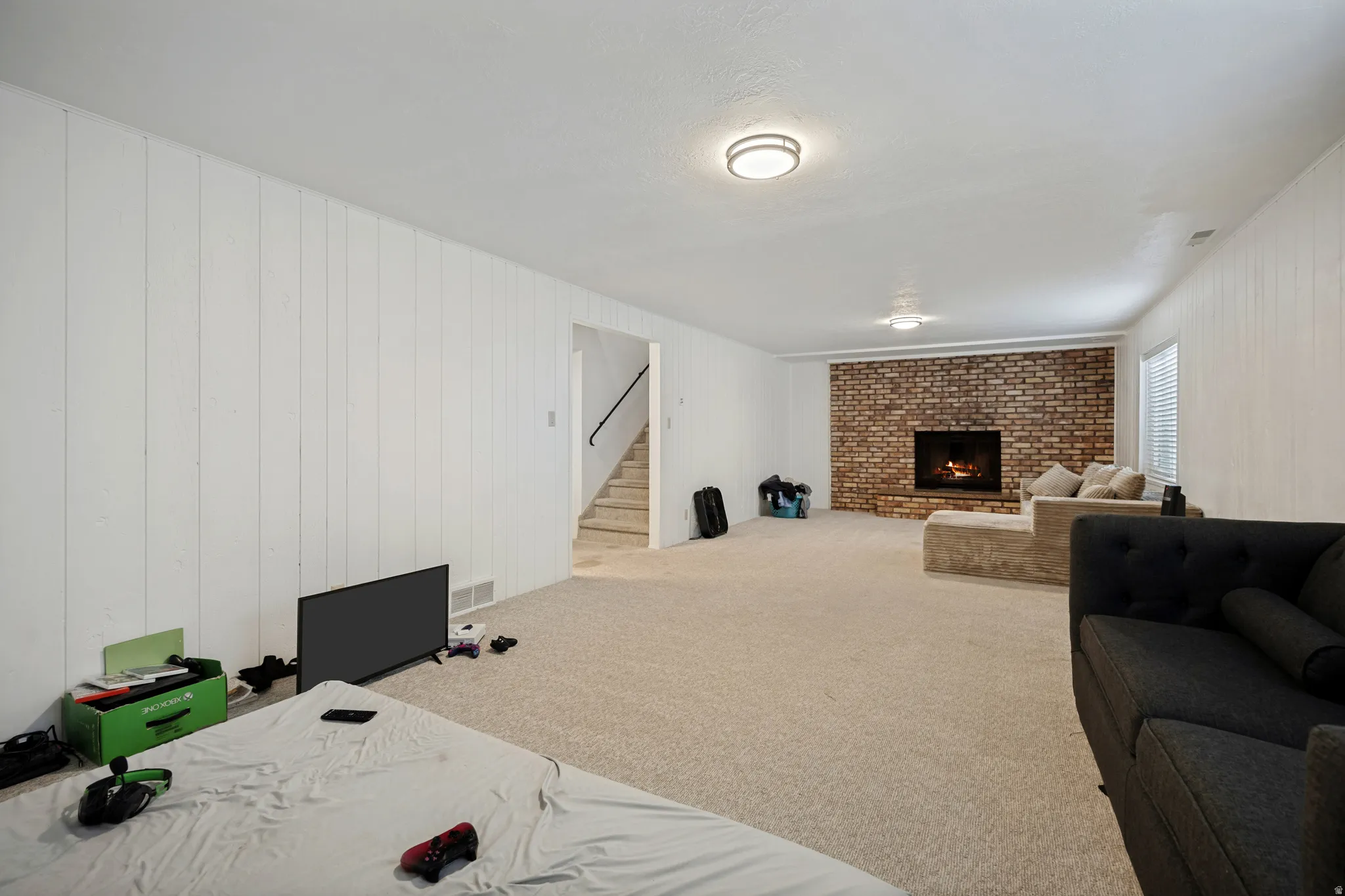 6711 - Basement Living Room. Spacious room featuring a brick-faced fireplace, white paneled walls, and neutral carpeting