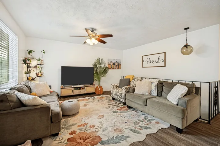 6711 - Living area featuring wood-finish flooring, a ceiling fan, and a built-in metal railing