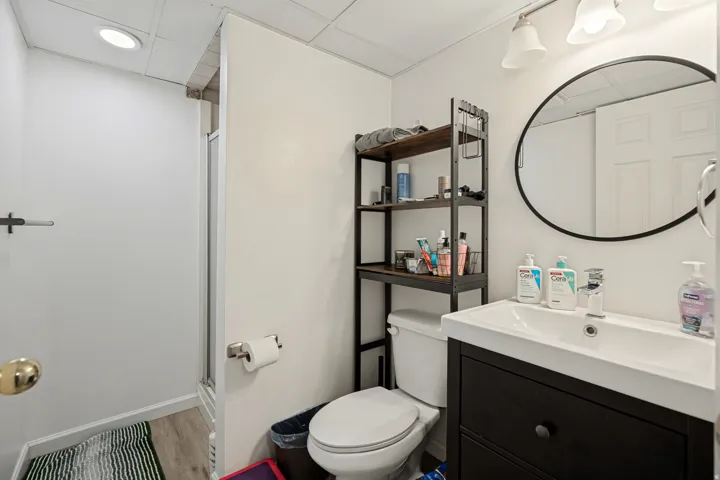 6711 - Basement Bathroom featuring a vanity with an integrated sink, round framed mirror, a three-light fixture, and a walk-in shower with a glass enclosure