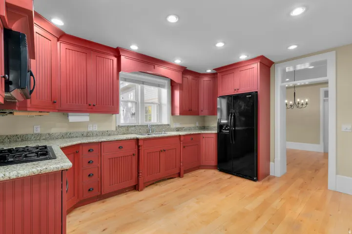Red wood-finish cabinetry, light-toned wood-finish flooring, recessed ceiling lighting, black built-in refrigerator, and stone-finish countertops