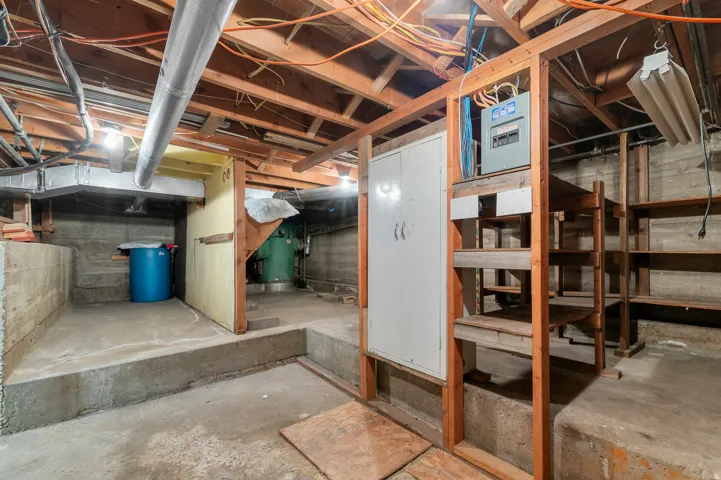 Exposed ceiling joists with overhead lighting, concrete flooring, and built-in wood shelving