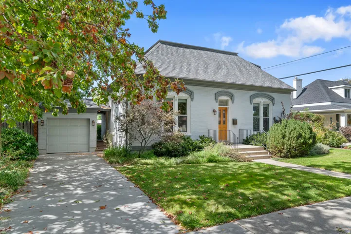 Brick exterior with arched window casings, inviting front porch, attached garage, and mature landscaping