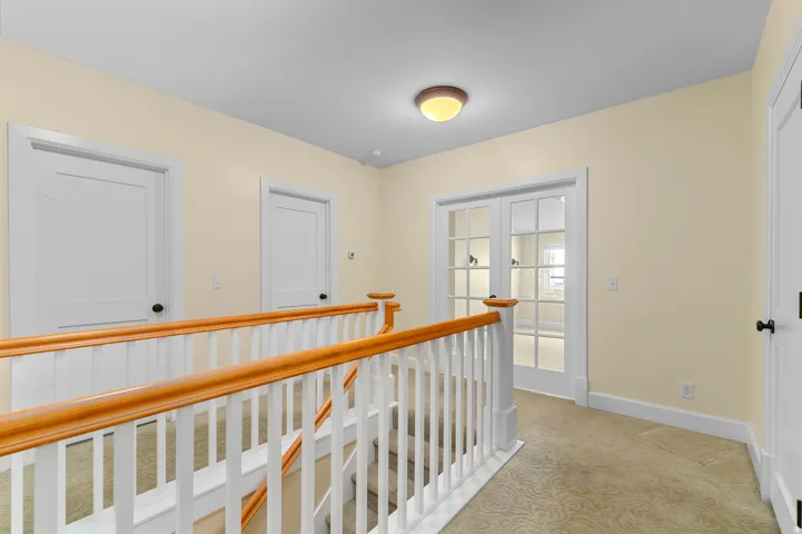 Neutral wall color, carpeted flooring, white trim, wood handrail, and French doors