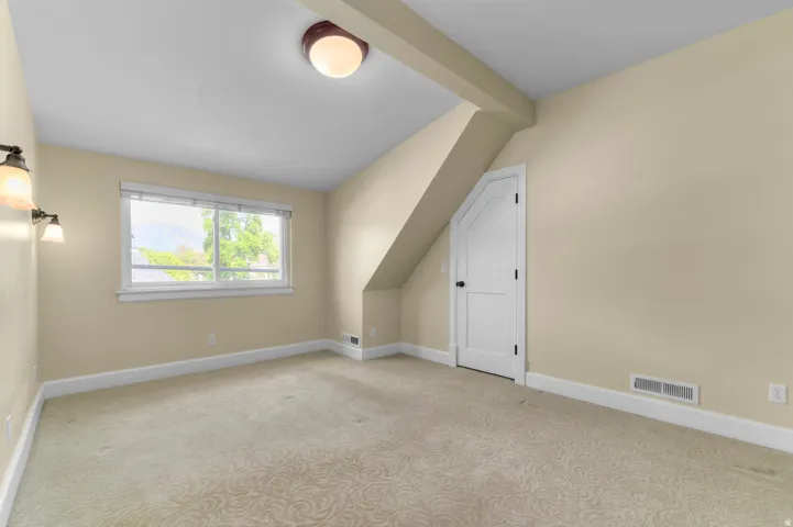 Carpeted room with a pitched ceiling and a window featuring a roller shade