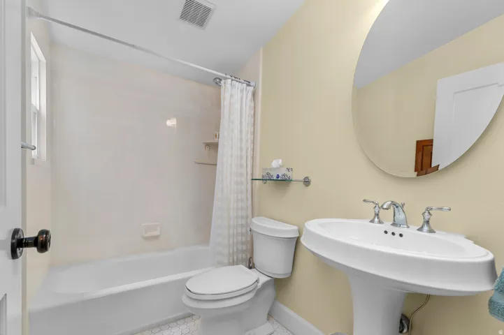 Bathroom featuring a pedestal sink with chrome fixtures, a shower/tub combination, a toilet, and an oval mirror