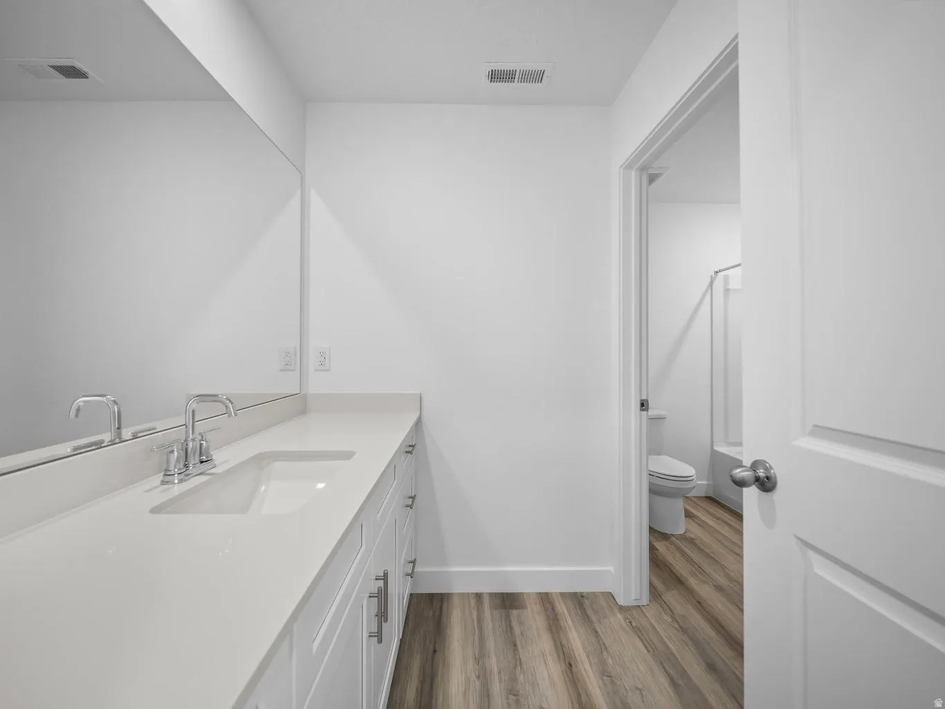 Vanity with an integrated sink, polished chrome faucet, expansive mirror, wood-finish flooring, and white cabinetry
