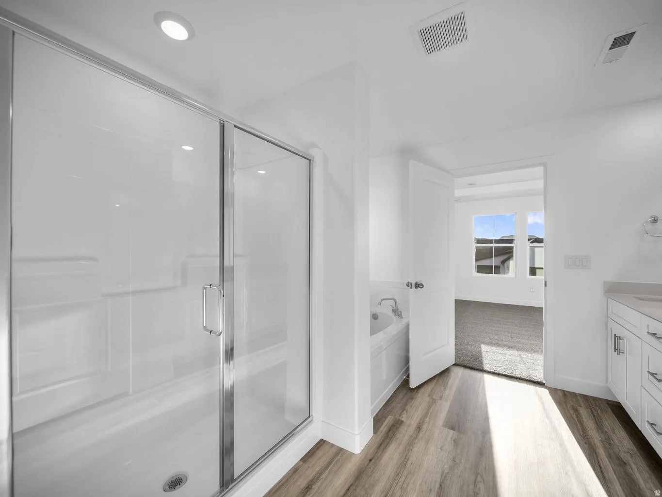 Glass-enclosed shower, built-in bathtub, light wood-finish flooring, white cabinetry, and recessed lighting