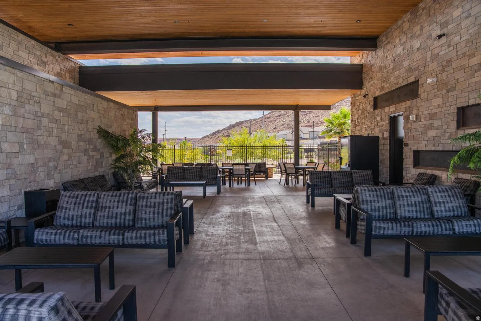 Expansive covered patio area featuring stone-clad walls, a wood-finish ceiling, and concrete flooring