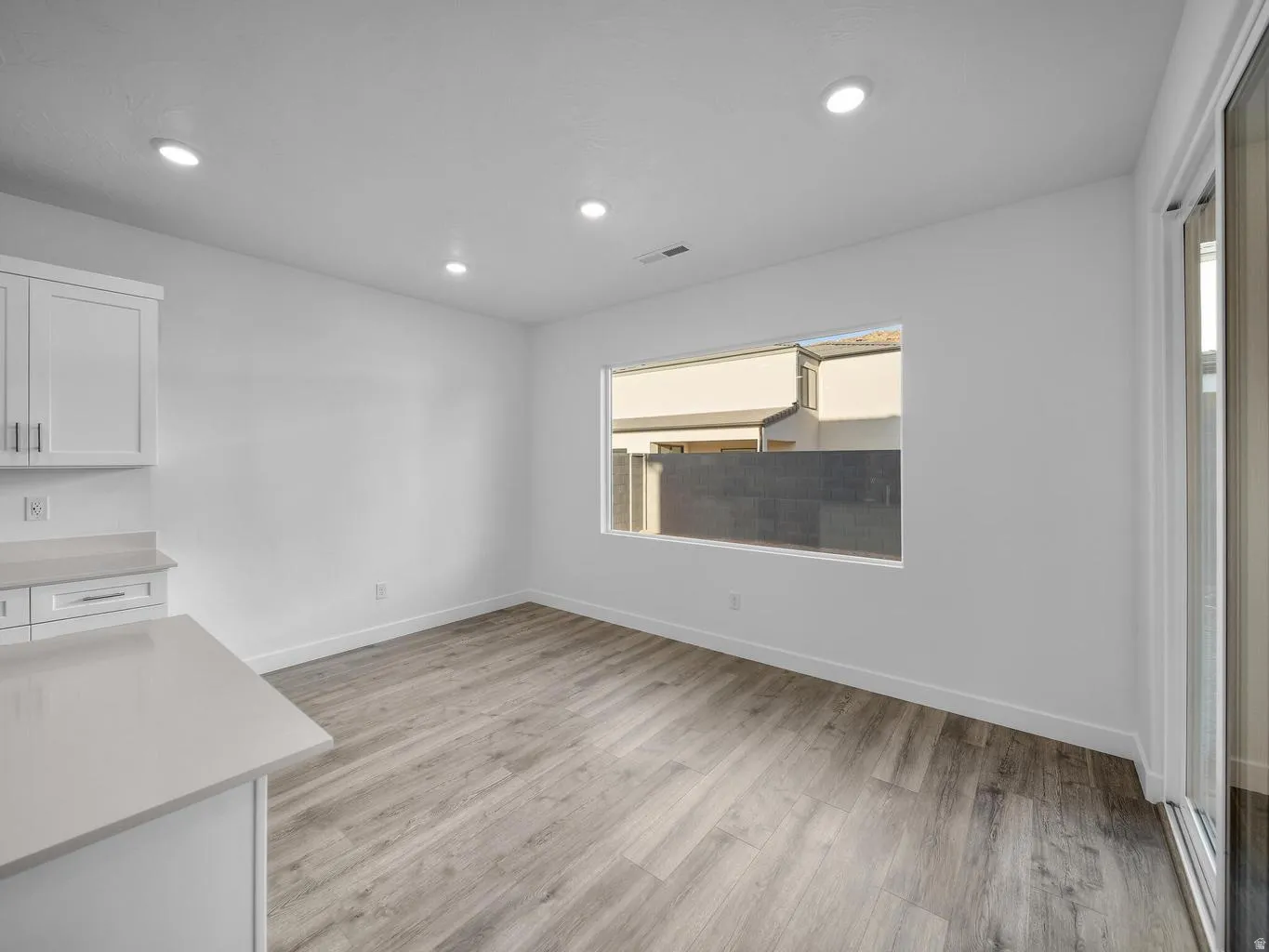Recessed lighting, wood-finish flooring, white cabinetry, light-toned countertop, and sliding glass door