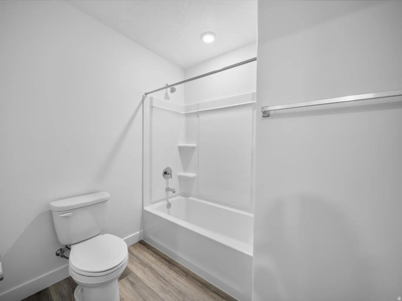 White porcelain toilet, wood-finish flooring, white shower/tub combination, chrome fixtures, and recessed ceiling lighting