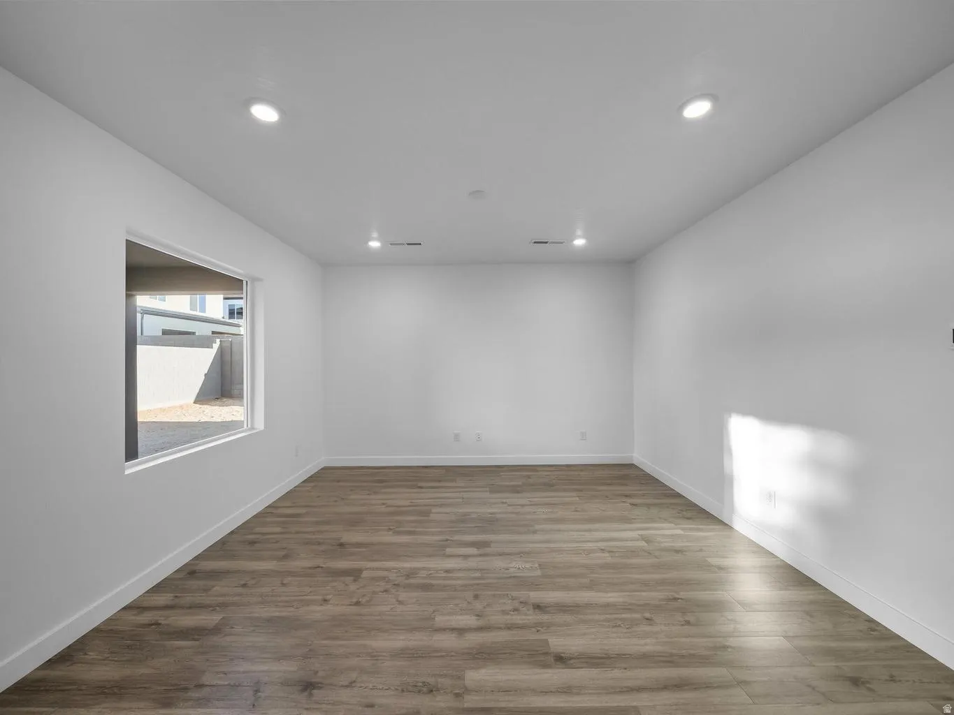 Recessed lighting, wood-finish flooring, white walls, and a large window