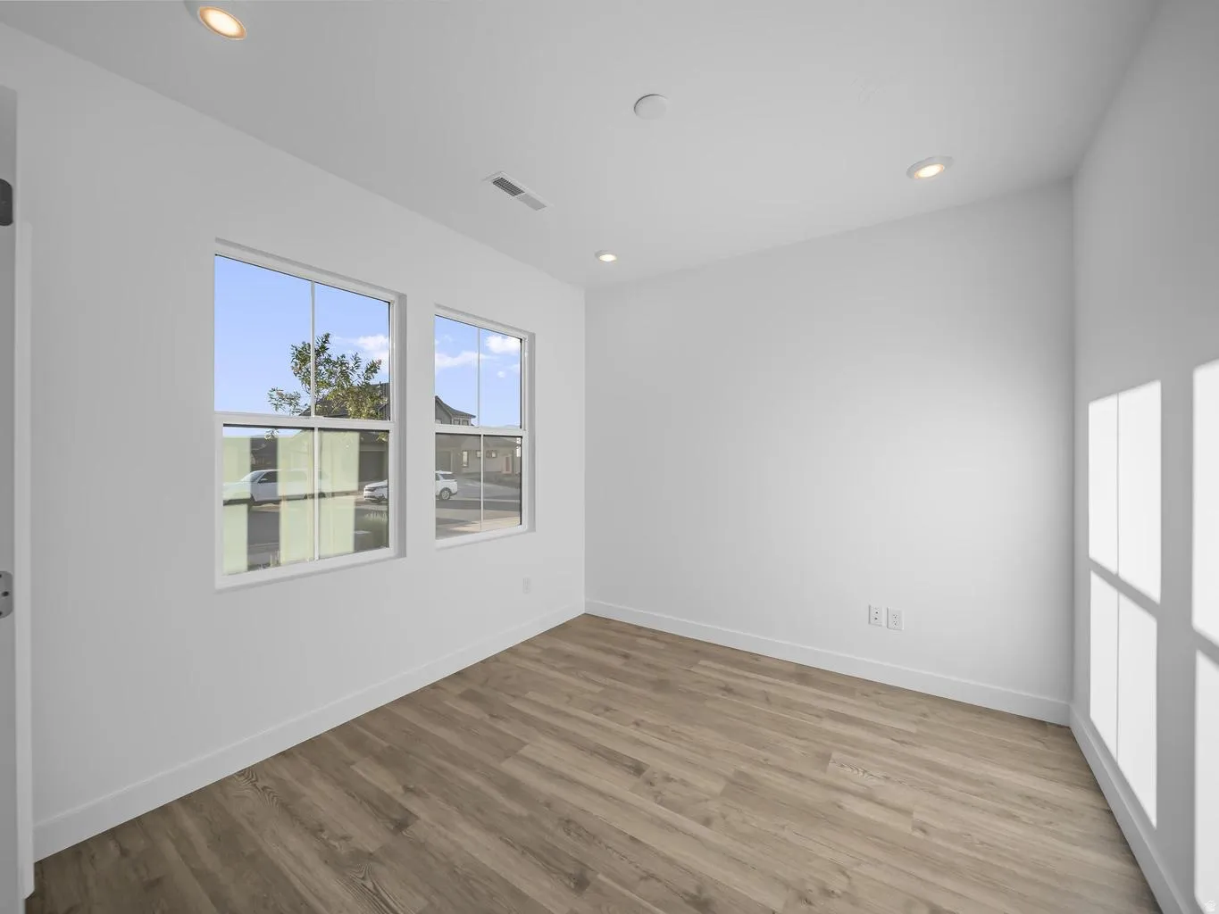 Recessed lighting, wood-finish flooring, and white walls with two windows